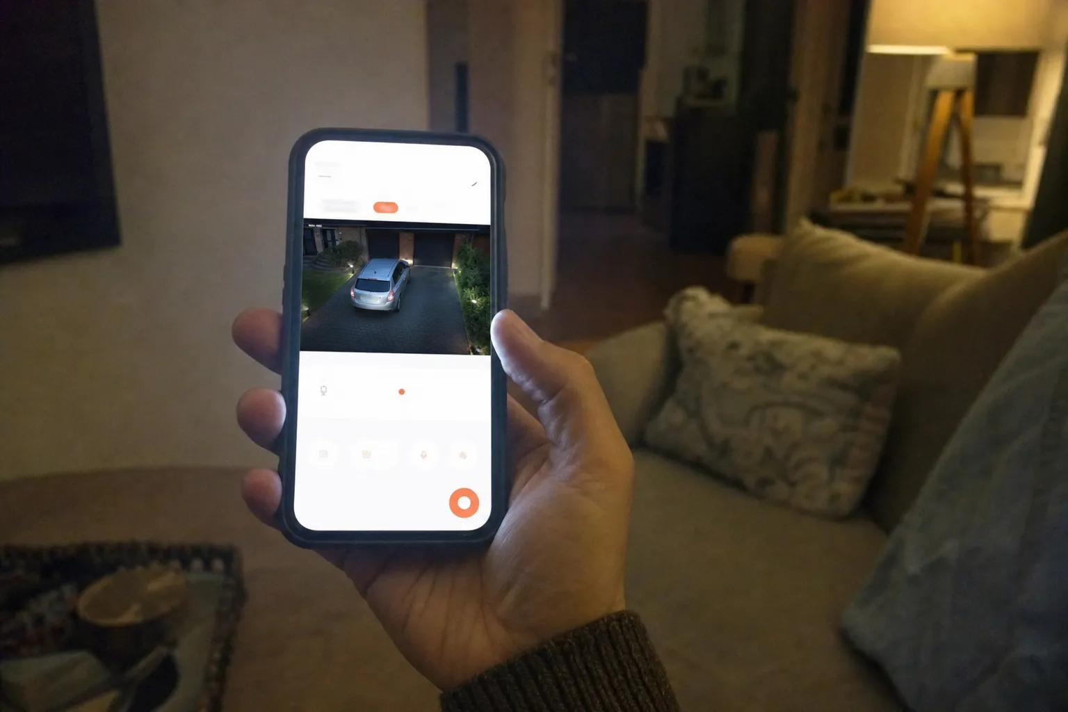 Hand hält Smartphone mit geöffneter Überwachungs-App und Livebild der Einfahrt